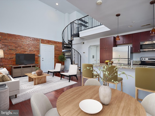 dining space with visible vents, wood finished floors, brick wall, a high ceiling, and stairway