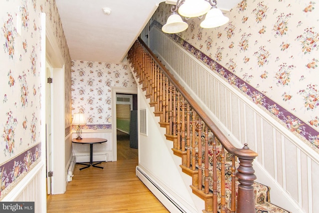staircase with a baseboard radiator, wainscoting, wallpapered walls, and wood finished floors