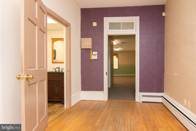 corridor with light wood-style floors, a sink, a baseboard heating unit, and wallpapered walls