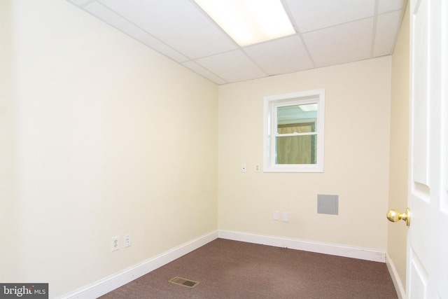 spare room with baseboards, a drop ceiling, dark carpet, and visible vents