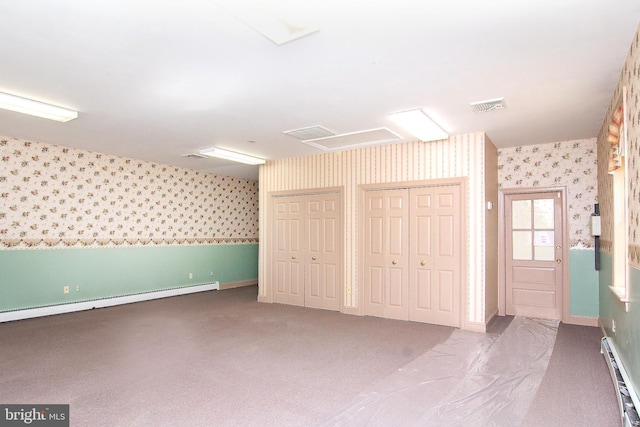 unfurnished bedroom featuring two closets, wallpapered walls, a baseboard heating unit, and attic access