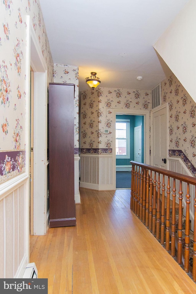 hall featuring visible vents, light wood-style flooring, a wainscoted wall, and wallpapered walls