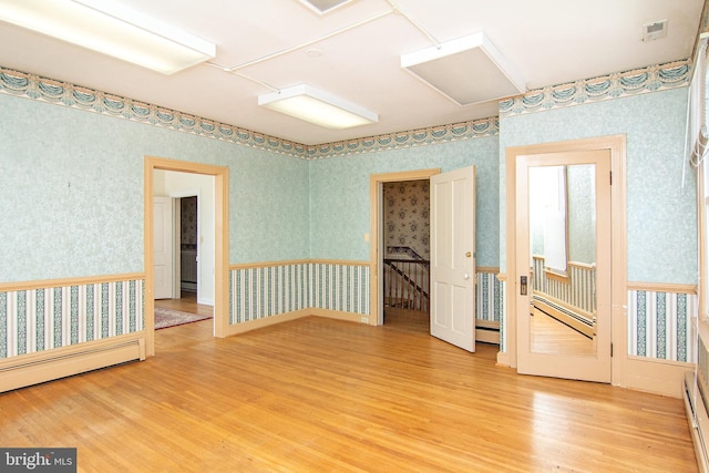 unfurnished room with a baseboard heating unit, wallpapered walls, wood finished floors, and visible vents