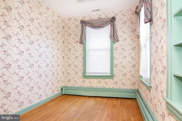 spare room featuring a healthy amount of sunlight, baseboards, a baseboard radiator, and wood finished floors