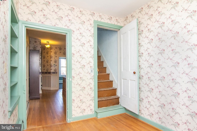 stairway with baseboards, wallpapered walls, and wood finished floors