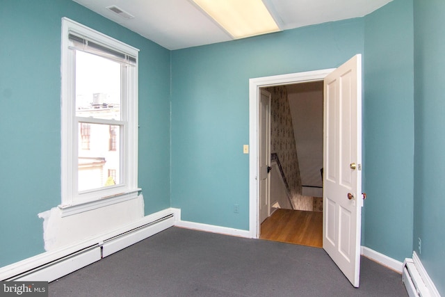 carpeted spare room featuring a healthy amount of sunlight, a baseboard radiator, and visible vents