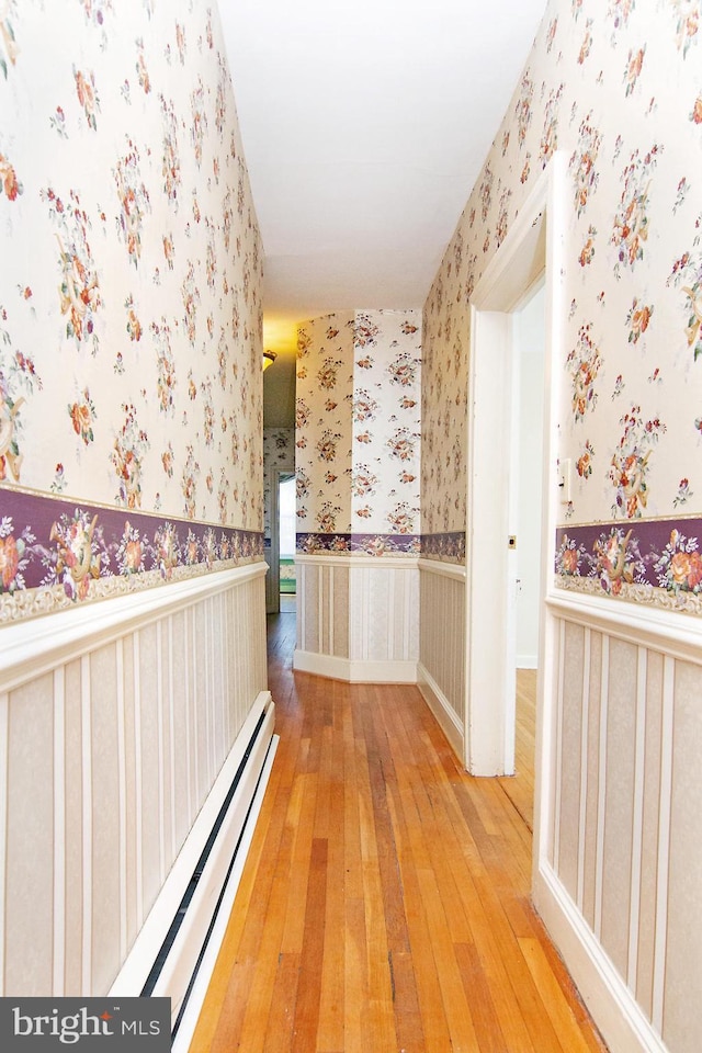 corridor with a baseboard radiator, wainscoting, wallpapered walls, and hardwood / wood-style floors