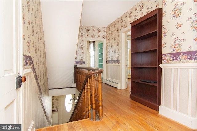 hall featuring hardwood / wood-style floors, wallpapered walls, a wainscoted wall, a baseboard radiator, and an upstairs landing