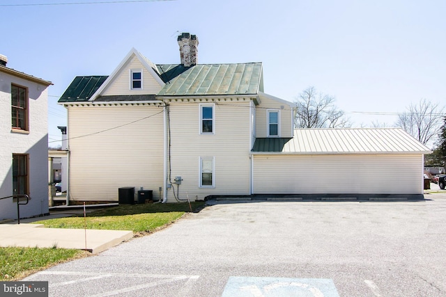 view of property exterior with central air condition unit, metal roof, a chimney, and a standing seam roof