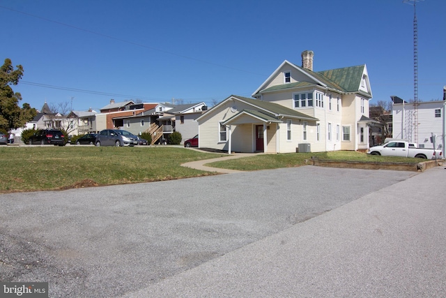 view of front of property with a chimney, a front lawn, central AC, and a residential view