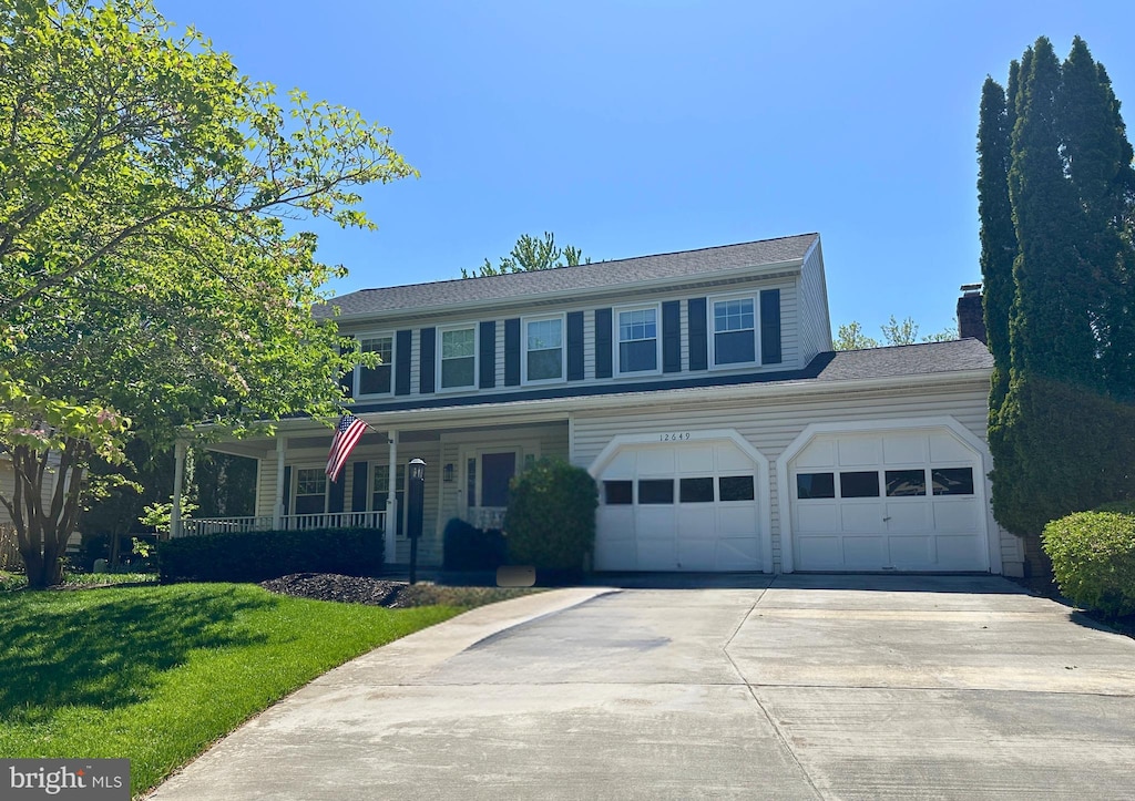 traditional-style home featuring a chimney, concrete driveway, a porch, and a front yard