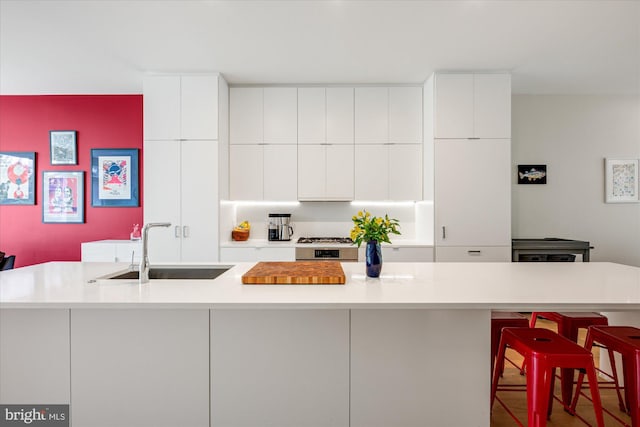 kitchen with a breakfast bar area, modern cabinets, a sink, light countertops, and white cabinetry