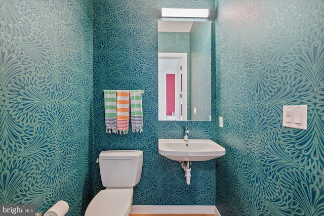 bathroom featuring a sink, toilet, and wallpapered walls