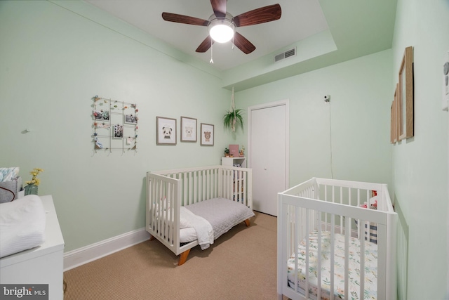 bedroom featuring visible vents, baseboards, ceiling fan, a crib, and carpet