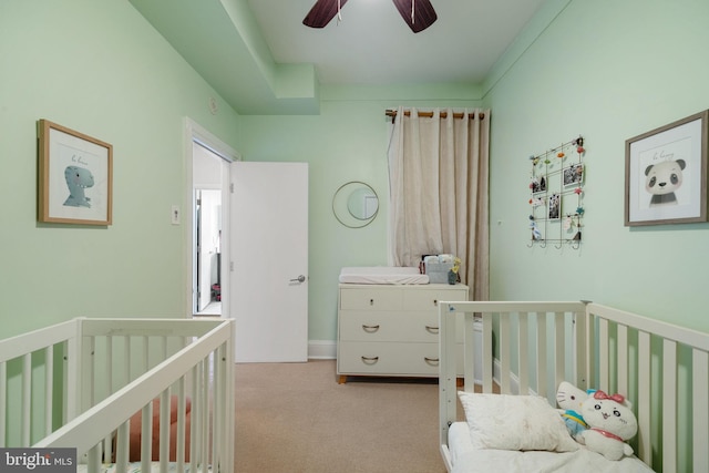 carpeted bedroom with a crib and ceiling fan