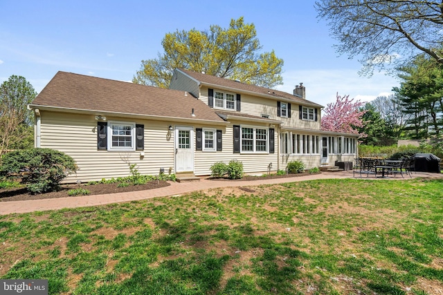 rear view of house with roof with shingles, entry steps, a chimney, a patio area, and a yard