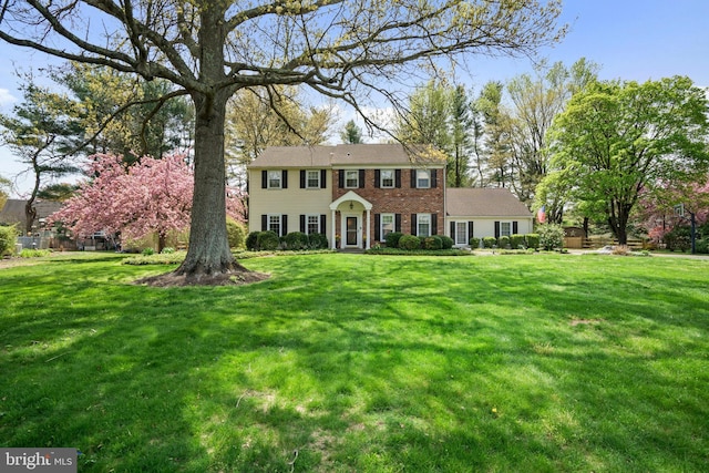 colonial inspired home with brick siding and a front yard