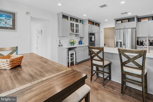 kitchen featuring decorative backsplash, a kitchen bar, visible vents, wood finished floors, and stainless steel fridge
