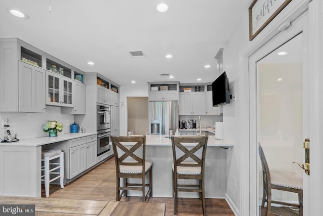 kitchen with light wood-type flooring, a peninsula, appliances with stainless steel finishes, and a kitchen bar