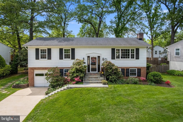 raised ranch featuring an attached garage, brick siding, a front yard, a chimney, and driveway