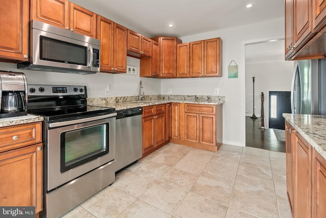 kitchen featuring brown cabinets, stainless steel appliances, light stone counters, and a sink