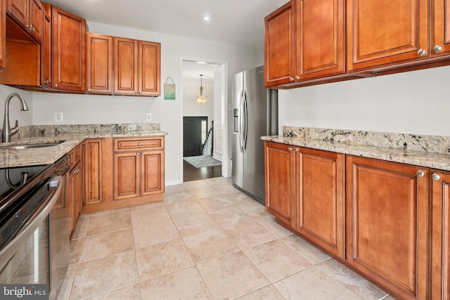 kitchen featuring appliances with stainless steel finishes, brown cabinetry, a sink, and light stone counters