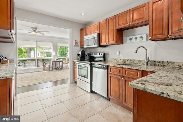 kitchen with brown cabinets, ceiling fan, light stone counters, a sink, and stainless steel appliances