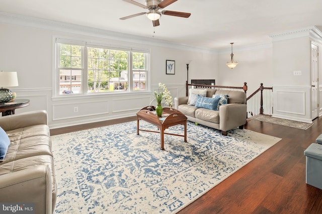 living area with ceiling fan, ornamental molding, wainscoting, and dark wood finished floors