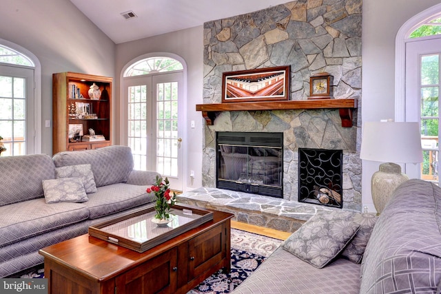 living area with visible vents, a stone fireplace, and lofted ceiling