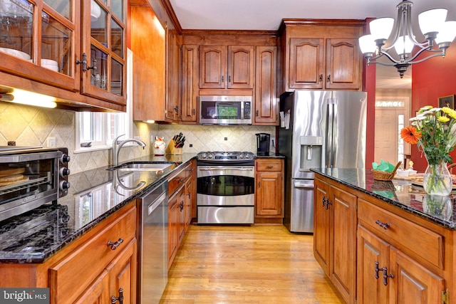 kitchen with brown cabinets, appliances with stainless steel finishes, a sink, dark stone countertops, and a toaster