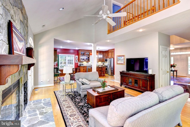 living area with a fireplace, light wood-style floors, high vaulted ceiling, a ceiling fan, and a healthy amount of sunlight
