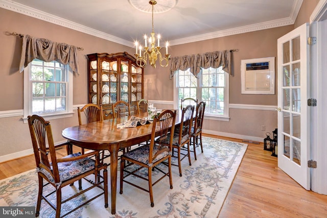 dining space with light wood-type flooring, ornamental molding, a notable chandelier, and a healthy amount of sunlight