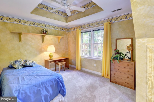 carpeted bedroom featuring a ceiling fan, a tray ceiling, visible vents, and baseboards