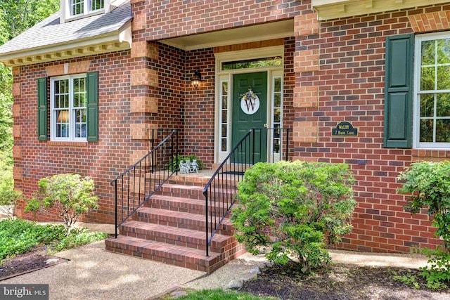 doorway to property with brick siding and roof with shingles