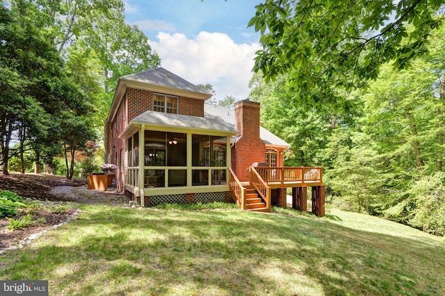 rear view of house featuring a wooden deck, a chimney, a sunroom, a shingled roof, and a lawn