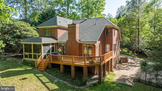 back of property with a chimney, a lawn, a deck, a sunroom, and a shingled roof