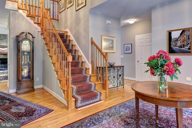 stairway featuring baseboards, a high ceiling, and wood finished floors