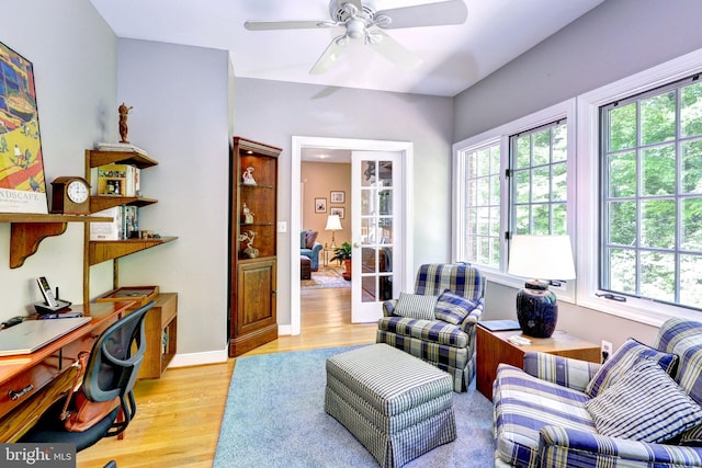 living room featuring baseboards, a ceiling fan, and light wood finished floors