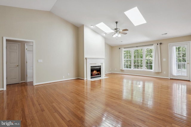 unfurnished living room with a skylight, a fireplace with flush hearth, high vaulted ceiling, and light wood-style floors