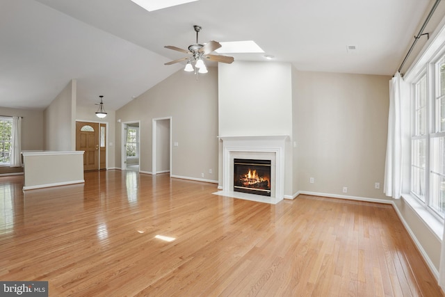 unfurnished living room with baseboards, ceiling fan, light wood-type flooring, a fireplace with flush hearth, and a skylight