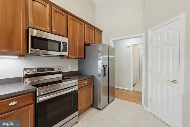 kitchen featuring washer / dryer, light tile patterned flooring, dark countertops, brown cabinets, and appliances with stainless steel finishes
