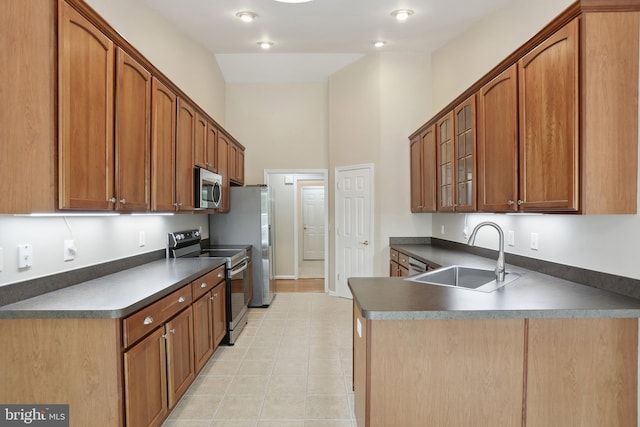 kitchen with appliances with stainless steel finishes, dark countertops, a sink, a peninsula, and glass insert cabinets