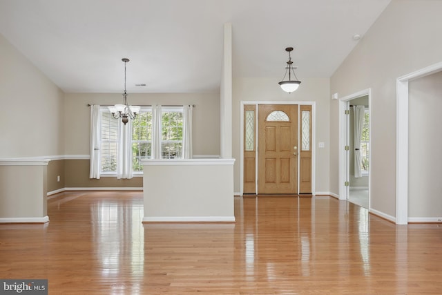 foyer entrance featuring baseboards, light wood-style flooring, and a notable chandelier
