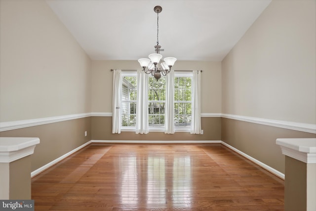 unfurnished dining area featuring baseboards, a notable chandelier, lofted ceiling, and hardwood / wood-style flooring