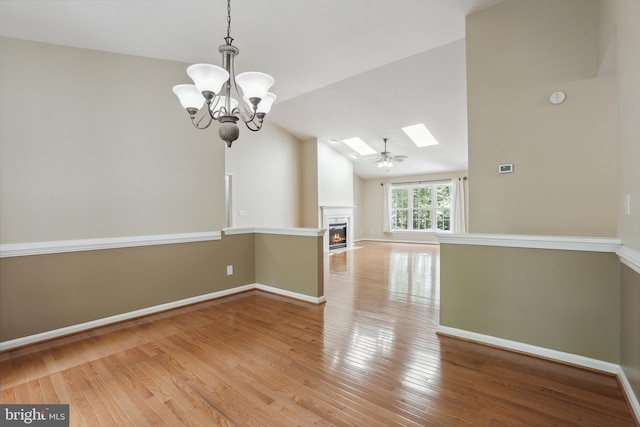 unfurnished dining area featuring a lit fireplace, baseboards, light wood finished floors, lofted ceiling with skylight, and an inviting chandelier