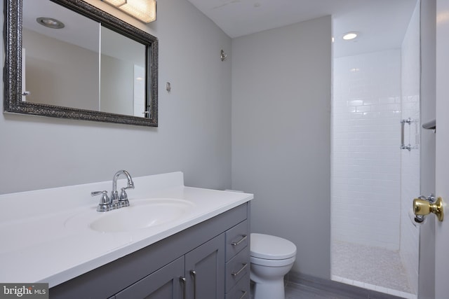 full bathroom featuring vanity, a tile shower, and toilet