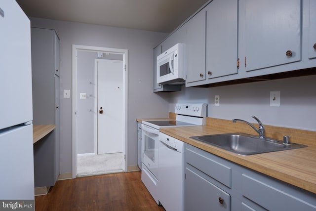 kitchen featuring a sink, baseboards, white appliances, and dark wood finished floors