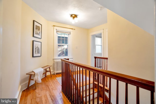 corridor with baseboards, an upstairs landing, radiator heating unit, and light wood-style floors