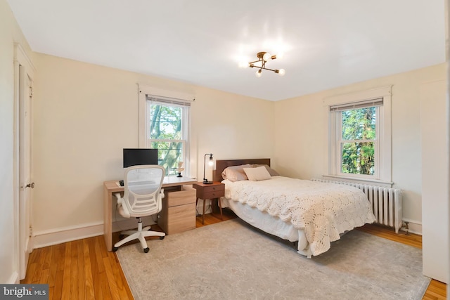 bedroom with wood finished floors, baseboards, radiator heating unit, and an inviting chandelier