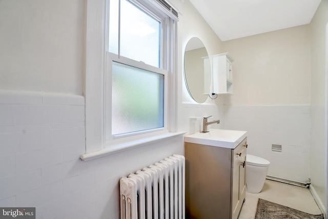 bathroom with radiator heating unit, tile walls, vanity, and a healthy amount of sunlight